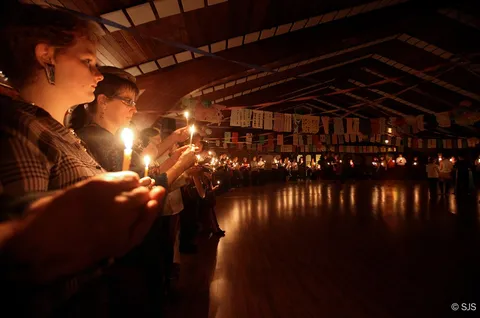 A large circle of people each holding candles in a dark room decorated with paper banners