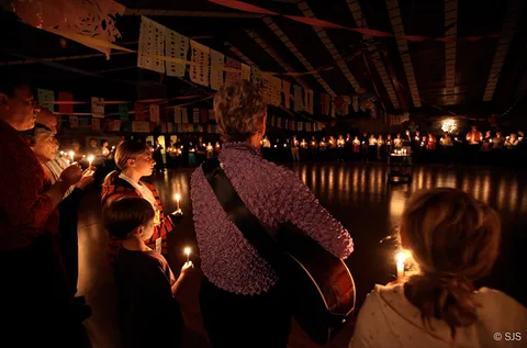 A wide view of a candlelit circle with a woman carrying a guitar and children holding candles nearby (Patricia Williams)