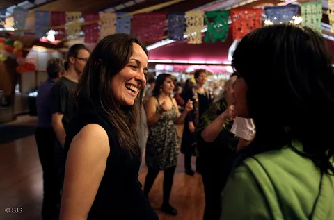 A smiling woman in focus with many other people in a bright hall decorated with paper banners (Birgit)