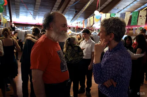 A bearded man and a woman conversing on a crowded dance floor (Henry and Patricia)