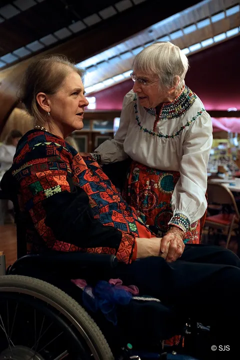 A woman in a wheelchair holding hands with an older woman in an embroidered blouse (Cindy Green and Helen Hardin)