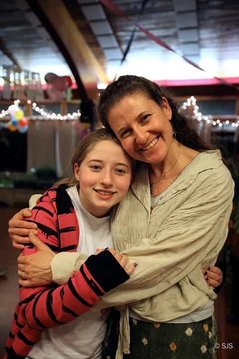 A girl and a woman with their heads together, both smiling, hugging indoors (Fiona and Deb)