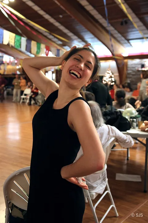 A young woman in a black dress laughs, hand on her head, in a decorated hall (Sophia)