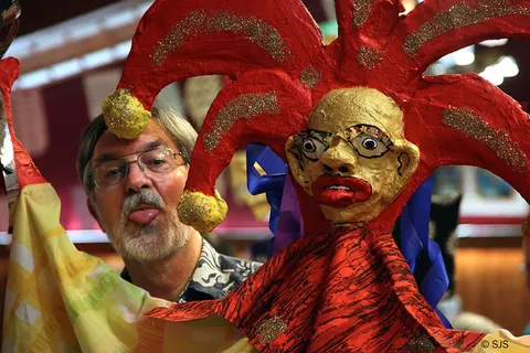 Close-up of a red and gold jester puppet head beside a bearded man making a face (Charlie Karl)
