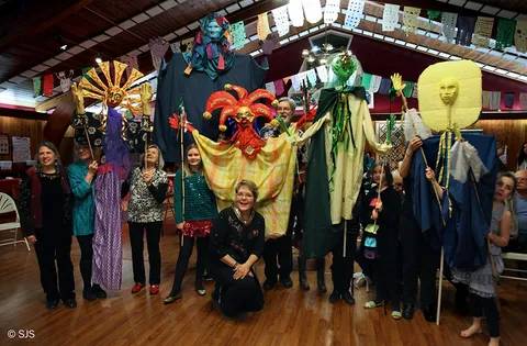 Group posing indoors with tall handmade puppet figures at a New Year's Eve puppet procession