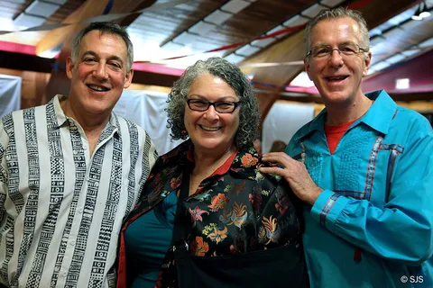Three adults smiling closely together at an indoor evening event (From left to right: David, Alison and Ed)